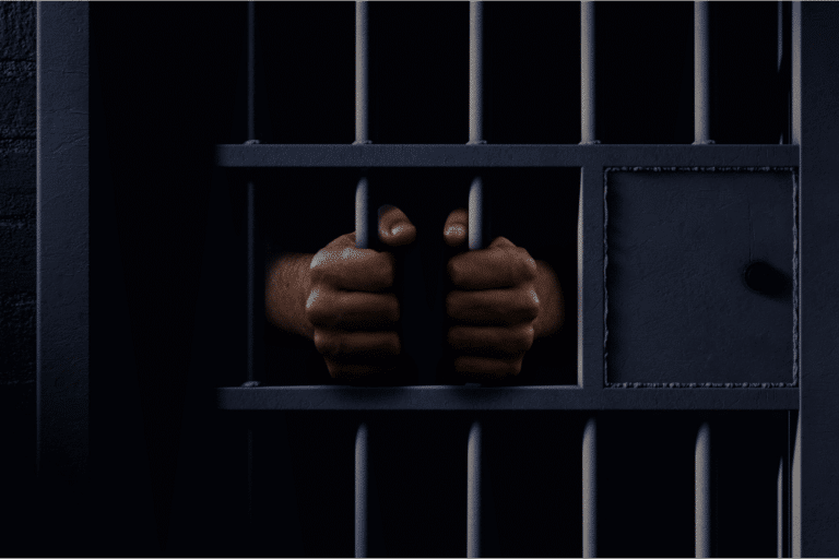 man in custody with his hands around jail cell bars