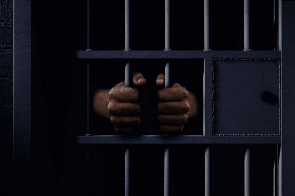 man in custody with his hands around jail cell bars