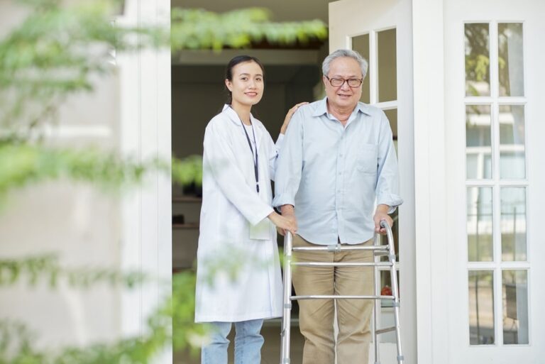Portrait of Asian senior man with walker walking outdoors together with Asian young nurse in a nursing home.