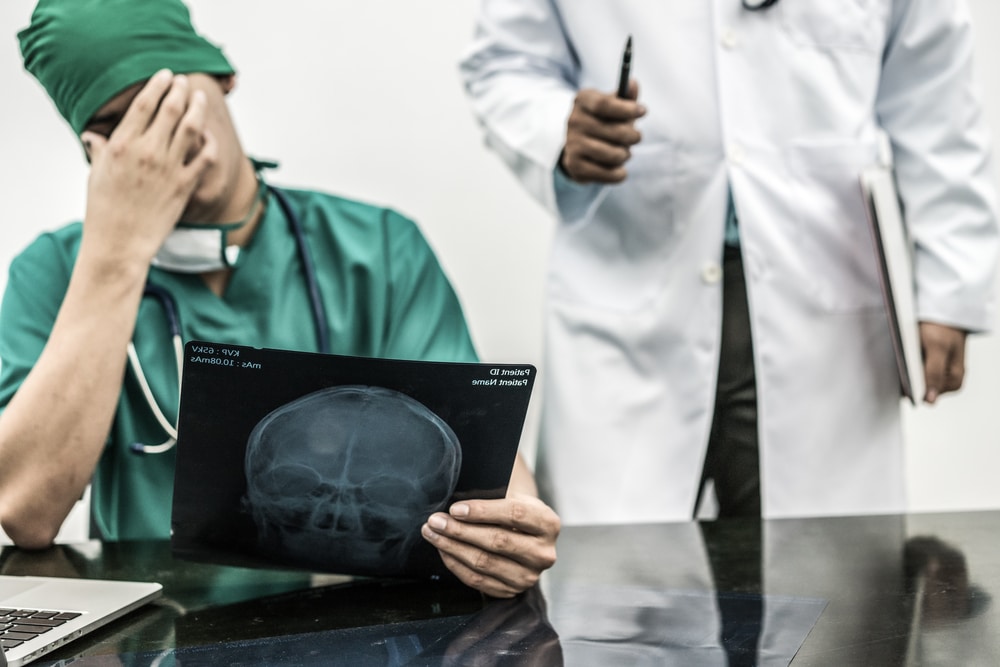 Surgical doctor covering his face with hand (face palm) expressing disappointment while holding x-ray film on office desk.