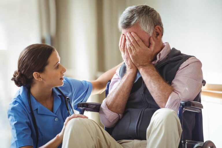A senior covering his face, and with a nurse