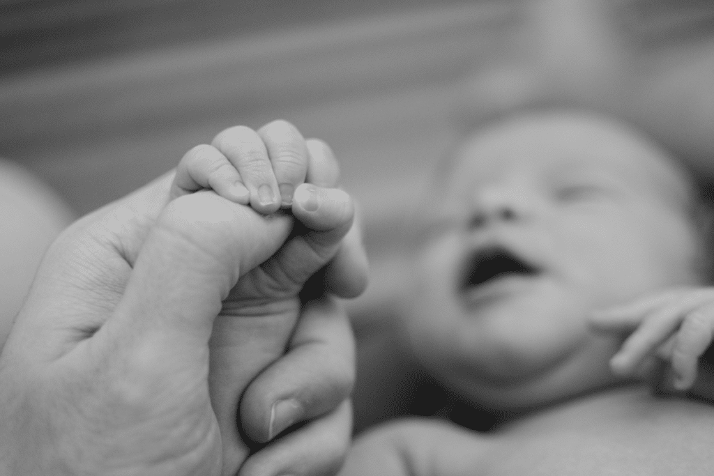 Greyscale photo of a newborn holding the hand of it's parent