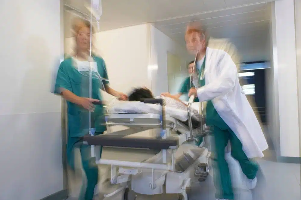 Healthcare workers including a doctor in a white coat, quickly pushing a patient on a hospital bed or stretcher