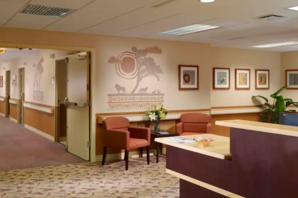A brightly lit room features two red armchairs and a small table with a vase of flowers in the center.