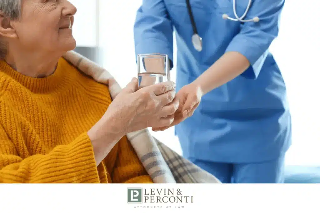 Nurse helping elderly patient in yellow sweater hold glass of water