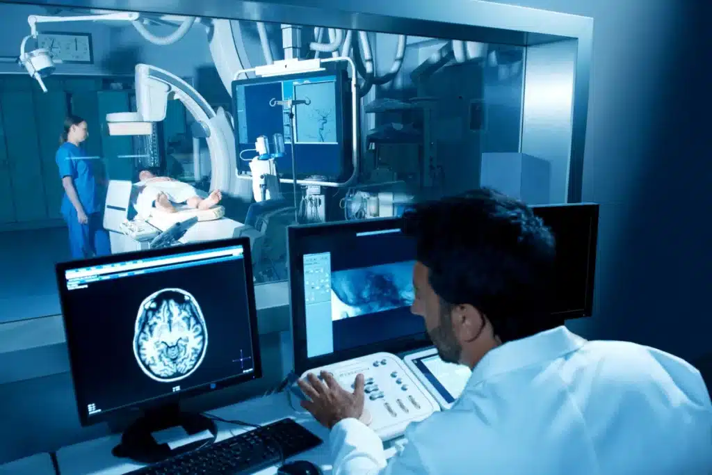 Radiologist reviewing brain MRI scans on multiple monitors while patient undergoes imaging procedure in hospital radiology department