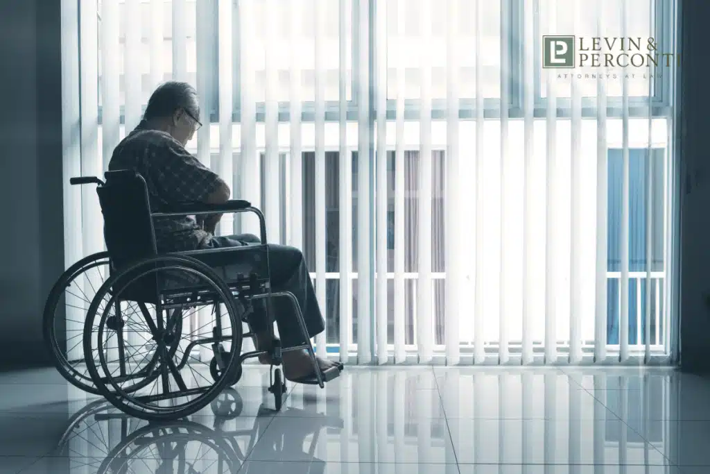 Elderly person in wheelchair looking out window of nursing home or medical facility with vertical blinds