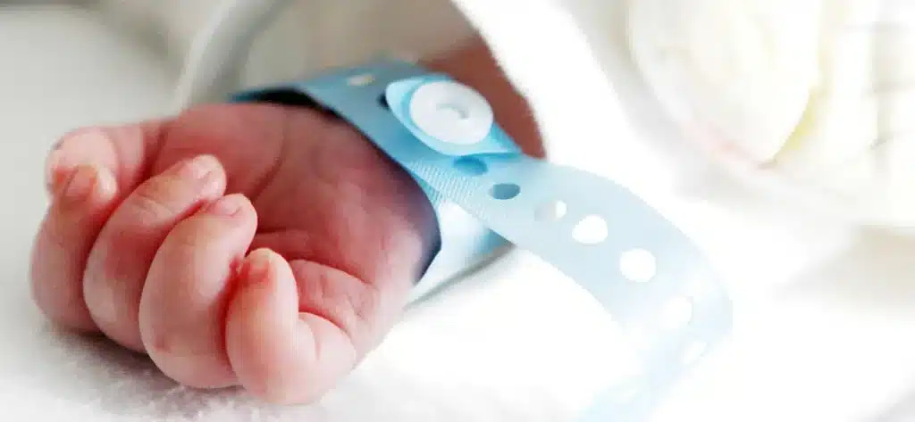 Close up of newborn baby's tiny hand with blue hospital identification bracelet on white blanket