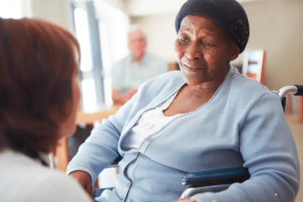 senior woman in wheelchair having conversation with healthcare provider or social worker in nursing home