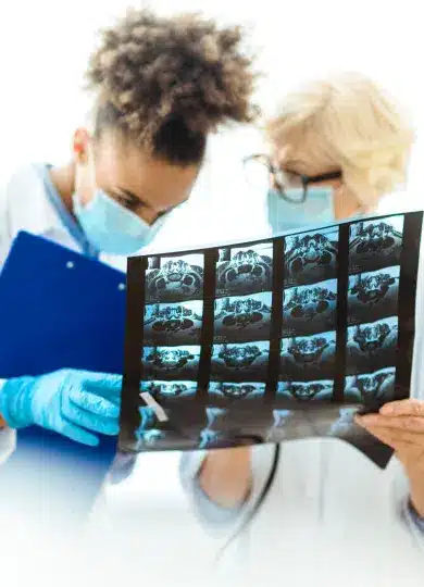 Two medical professionals in scrubs examining dental or medical X-ray images on light board during diagnosis