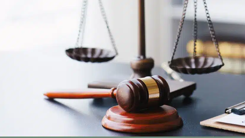 Wooden judge's gavel resting on sound block with brass scales of justice in background on courtroom table