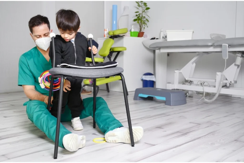 Physical therapist in green scrubs helping young child with mobility assistance using walking support equipment