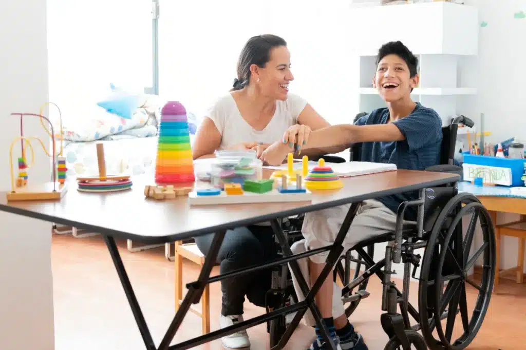 Smiling therapist and young boy in wheelchair playing with colorful stacking toys during occupational therapy session