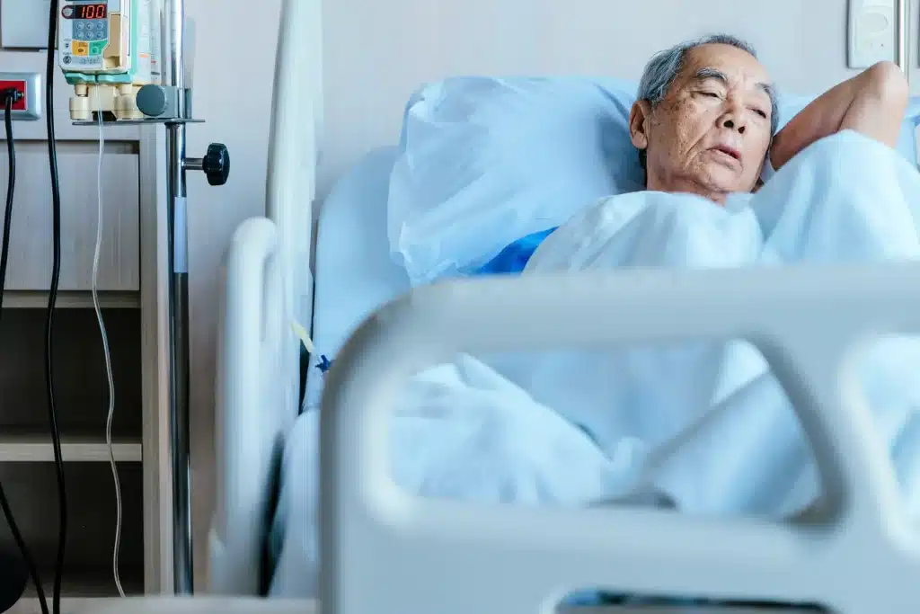 Elderly patient lying in hospital bed with IV pole and medical equipment