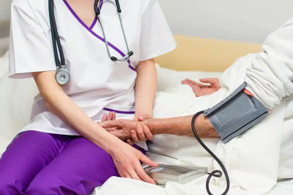 Nurse in purple scrubs taking elderly patient's blood pressure during medical examination in hospital room