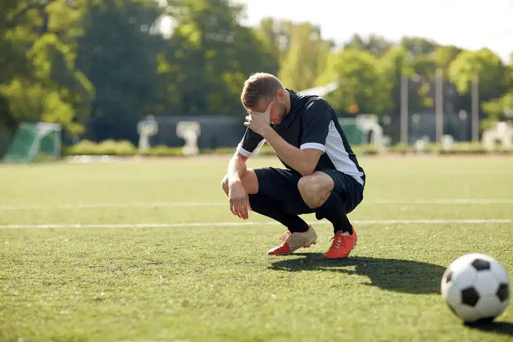 College athlete in mental distress, standing on a soccer field with his hand covering his face