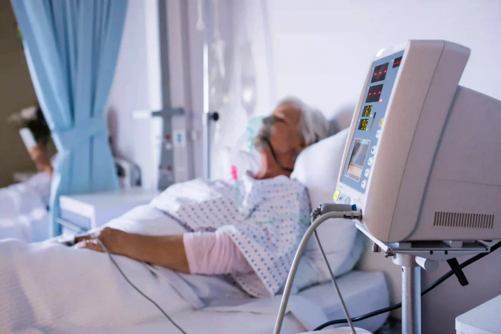 Elderly female patient with oxygen mask in hospital bed with vital signs monitor displaying heart rate