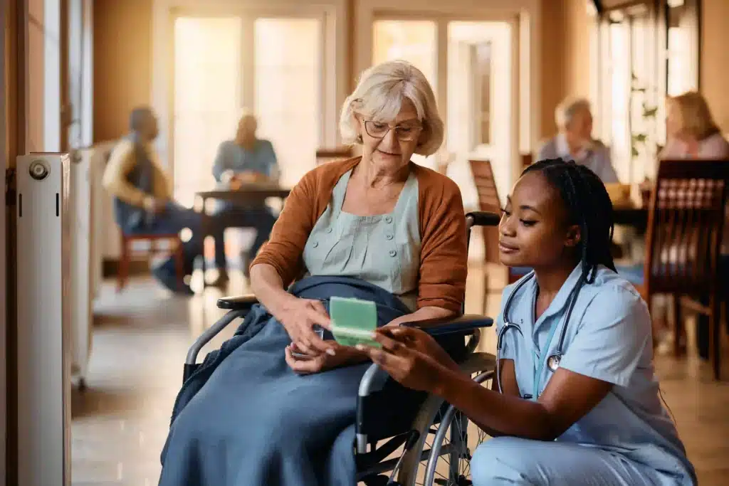 Elderly woman in a wheelchair receiving medication from a nurse at a nursing facility