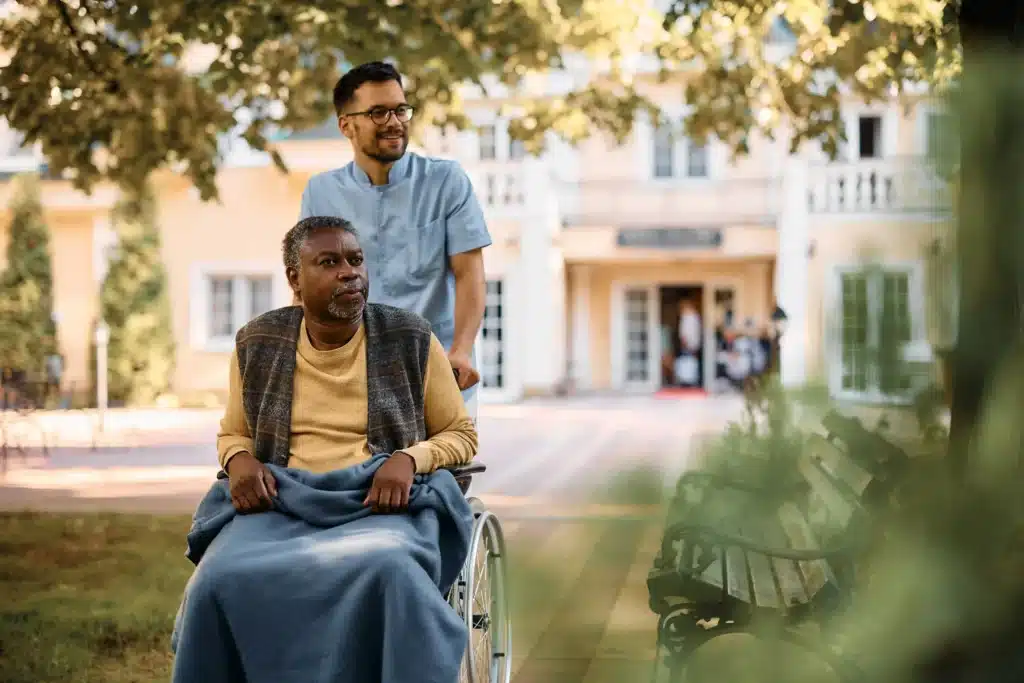 young-healthcare-worker-pushing-senior-black-man-in a nursing home