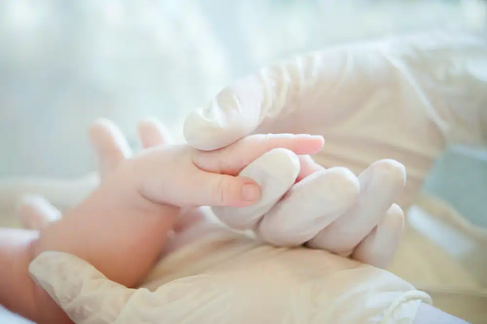 gloved hand of a medical professional holding a newborn's hand