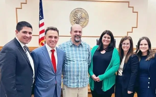 Legal team and client posing together in front of official seal and American flag
