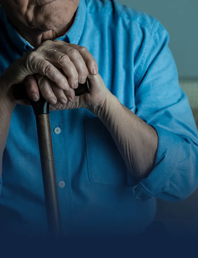 Elderly person's hands resting on walking cane while wearing blue shirt