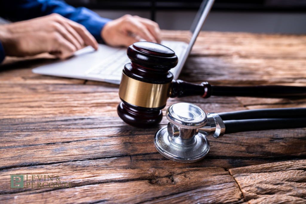 Gavel and stethoscope on a wooden desk with a person typing on a laptop unfocused in the background