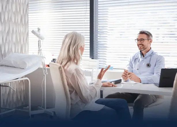 Mature Female Patient In Consultation With Doctor Sitting At Desk In Office