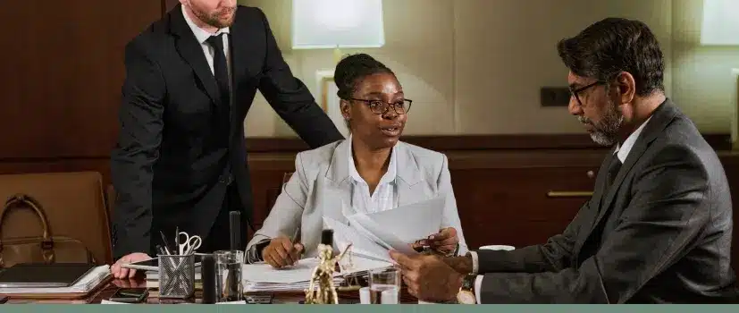 Three legal professionals in business attire collaborating over documents in law office conference room