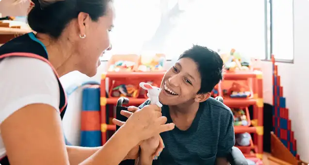 Therapist engaging smiling child with toy during therapy session in colorful playroom
