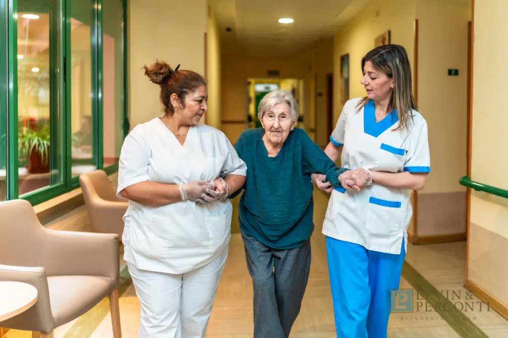 Two nursing home staff helping a resident walk down a hallway of a nursing home facility